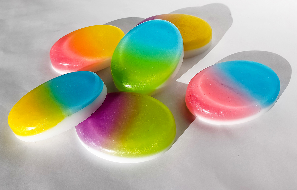 Ombré soap with a colour gradient and a white layer at the bottom is placed in several oval pieces on a white background.